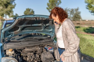 Kıdemli kadın araba kaputu açık bir şekilde yol yardımı istiyor.