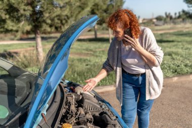Yol kenarındaki bozuk araba motorunu kontrol ederken kıdemli kadın yardım istiyor.
