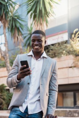 Gülümseyen Afrikalı Amerikalı iş adamı şehir ortamında akıllı telefon kullanıyor