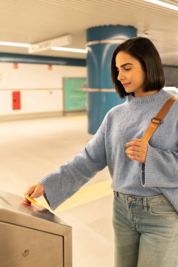 Metro girişinde toplu taşıma kartı kullanan genç bir kadın.