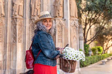 Bisikletli son sınıf öğrencisi kadın kameraya gülümserken akıllı telefon kullanıyor.