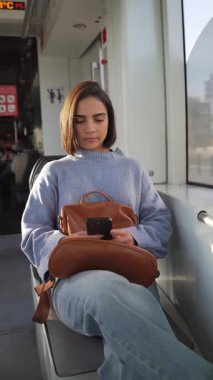 Latin kökenli genç bir kadın akıllı telefonunu kullanırken trenle gidip geliyor.