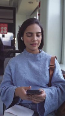Otobüste ya da trende giderken akıllı telefon ve kablosuz kulaklık kullanan mutlu bir kız öğrenci.