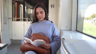 Pencerenin kenarında oturan genç bir kadın toplu taşıma hakkında bir kitap okuyor.