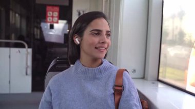 Kablosuz kulaklıklarla müzik dinleyen genç bir kadın toplu taşıma araçlarına binerken