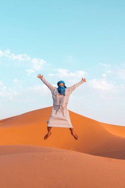 Berber adam geleneksel kıyafetleriyle Sahra Çölü, Fas 'ta kum tepelerine atlıyor.