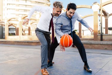 Dışarıda basketbol oynayan gömlekli ve kravatlı iki iş arkadaşı.
