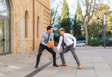 Takım elbiseli iki girişimci tatilde dışarıda basketbol oynarken eğleniyor.