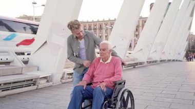Torunuyla tekerlekli sandalyedeki yaşlı adam bir şehir köprüsünü geçiyor.