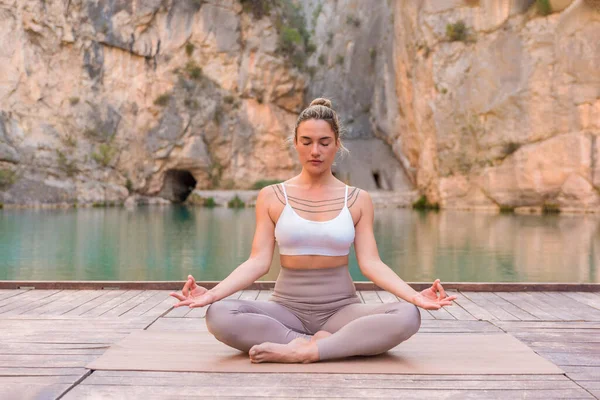 Kadının yoga ve meditasyon yaptığını göl kenarında, doğada huzurun ve farkındalığın tadını çıkardığını görmek.