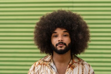 Yeşil arka planda afro saç stili ve sakallı gülümseyen melez bir adamın portresi.