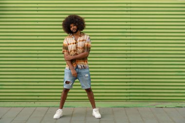 Yeşil duvarda duran afro saçlı şık bir adam.