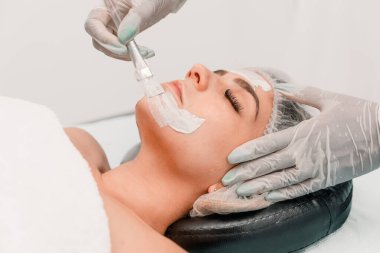 Güzellik uzmanının elleri kaplıcadaki genç bir kadına nemlendirici yüz maskesi uyguluyor.