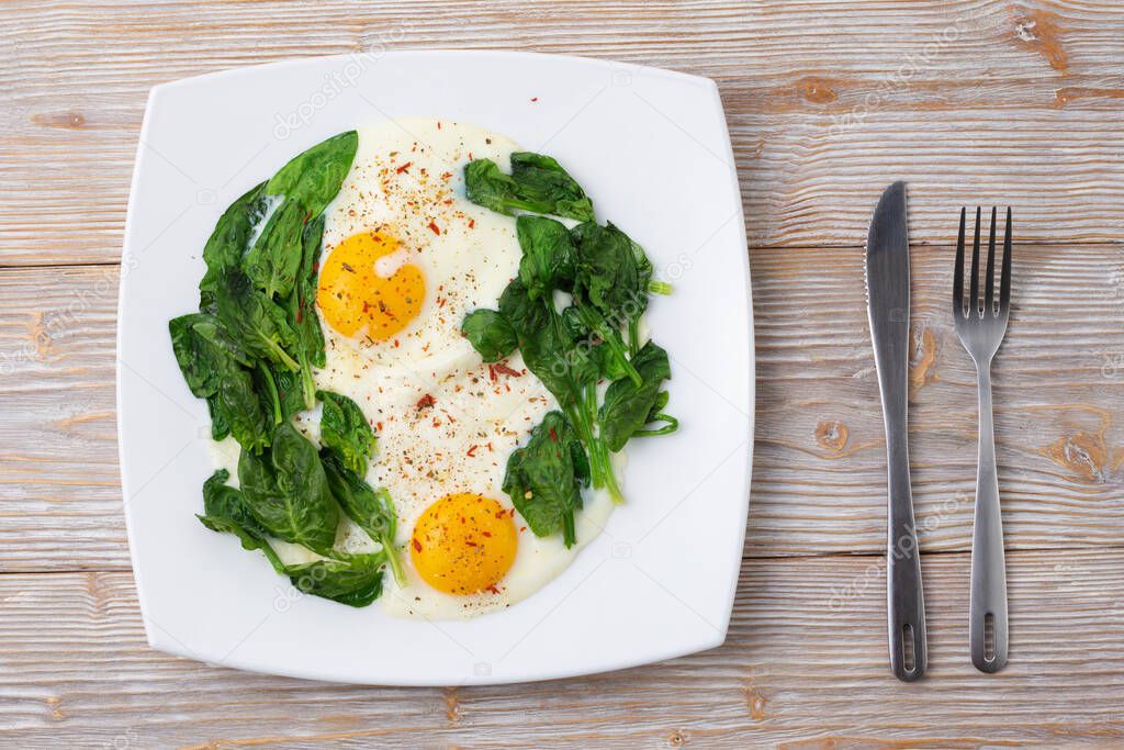 Plate with scrambled eggs and spinach on a wooden background, knife and fork. Top view flat layout. 