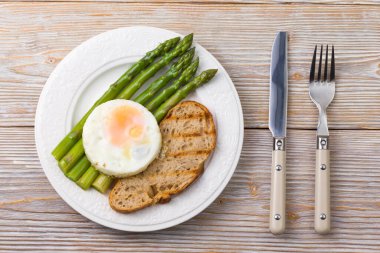 Çırpılmış yumurtalı kuşkonmaz ve çatal ve bıçaklı bir tabakta karabuğday ekmeği.