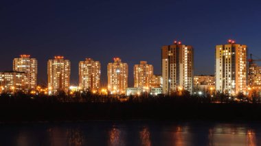 Güzel şehir manzarası. Kıyı şeridi boyunca sıra sıra dizilmiş çok katlı modern binalarla dolu yoğun nüfuslu yerleşim bölgesi ve akşam alacakaranlığı sokak ışıkları