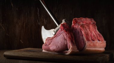 Mutfak baltası ile doğranmış taze çiğ domuz filetosu kesme tahtasının üzerinde gölgede eski kahverengi ahşap zemin ile duruyor. Yan görünüş. Sanatsal karamsar fotoğraf kopyalama alanı ile basit kırsal biçimdeName