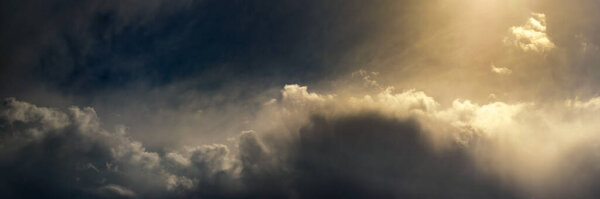 wide panoramic view of a dramatic sky with cumulus clouds and bright sunlight