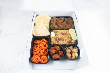 Iftar Meal Box South Asian Catering with Paratha Slice, Meat Biryani, Beef Curry, Flatbread, Chicken Malai Tikka Boti, and Jalebi isolated on marble background top view