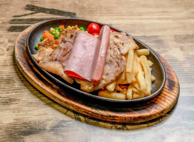 Sizzling Karışık Biftek Izgara Tavuk, Jambon, Sosis, Patates ve Sebzeler ahşap bir tahta yan görünümde sıcak dökme demir tavada servis ediliyor.