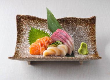 Dekoratif bir tabakta wasabi ile servis edilen taze somon, ton balığı ve istiridye içeren nefis sashimi tabağı otantik bir Japon yemek deneyimi vaat ediyor.