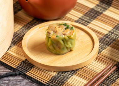 Sebzeli lezzetli Siu Mai ya da lezzetli bir yemek için shumai dim sum, arka planda yemek çubukları ve çay demliği ile bambu tepsisinde servis edilir.