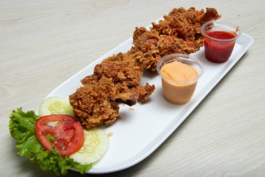 Lezzetli bir yemek için yanında taze marul, domates ve salatalık dilimleri ile birlikte kremalı sos ve ketçap ile servis edilen kızarmış tavuk lolipop parçaları..