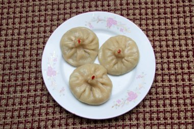 Tavuk Momos, kırmızı baharatlı hamur köftelerini beyaz bir çiçek tabağında sunar. Mutfak ilhamı ve yemek blogları için mükemmeldir.