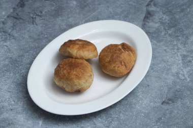 Lezzetli mutfak cazibesi için dokulu gri bir arka planda, mükemmel kızartılmış ve beyaz oval bir tabakta sunulan altın sarısı, tuzlu ekmek hamur işleri.