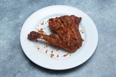 Kızarmış tavuk budu tikka ve kalça beyaz bir tabakta servis edilir, dağınık baharatlar ve kırıntılarla.