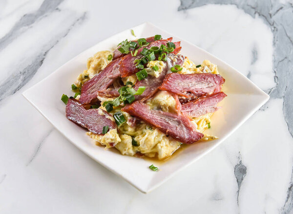 Delicious scrambled eggs topped with vibrant char siu pork and fresh scallions on a modern white plate perfect for brunch ads