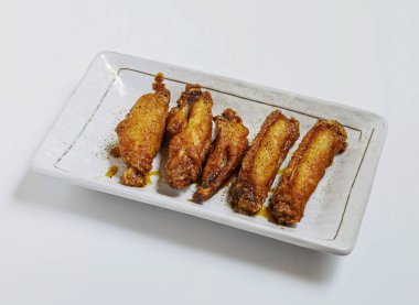 Zarif beyaz tabakta servis edilen altın sarısı tavuk kanatları öğle veya akşam yemeği için hazır. Atıştırma günü için mükemmel.