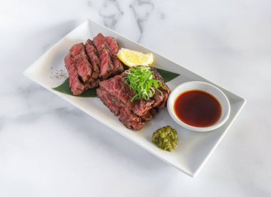 Canlı yeşil soğanlı kurutulmuş biftek tataki ve keskin bir limon dilimi, aşçılar için bir mutfak lezzeti.