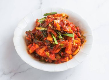 Baharatlı Kore turplu kimchi, kkakdugi, beyaz bir kasede servis edilir mermer bir yüzey üzerinde oturarak tat alma duyunuzu keyiflendirir.