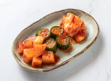 Canlı ve iştah açıcı bir kimçi ve salatalık kabı sade beyaz mermer bir yüzey üzerinde seramik bir kasede servis edilir. Mutfak ve yiyecekle ilgili projeler için mükemmeldir.