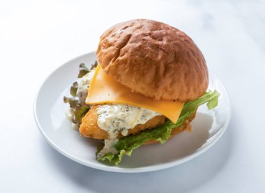 Ağız sulandıran bir balık sandviçi, erimiş peynir ve kremalı sos, temiz beyaz tabakta, hızlı ve lezzetli bir yemek için mükemmel.