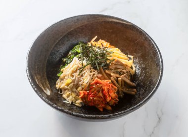 Canlı ve iştah açıcı Kore erişte kasesi kimçi ve yosunla dolu, parlak bir mermer masada sunuluyor, sağlıklı ve lezzetli bir akşam yemeği hissi uyandırıyor.