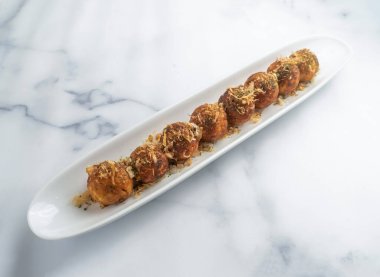 Beyaz bir tabakta servis edilen lezzetli takoyaki toplarının tadını çıkarın. Üstünde çıtır çıtır tempura parçaları ve lezzetli baharatlar var. Japon yemek aşıkları için mükemmel.