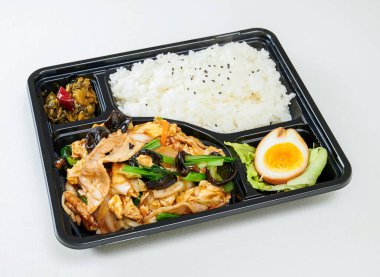 Ağız sulandıran Kore usulü domuz eti ve lezzetli taze sebzelerle dolu ahşap kulaklı bento kutusu ve beyaz arka planda beyaz pirinç ile servis edilen haşlanmış yumurta.