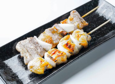 Sivri siyah tabakta soğanlı ızgara domuz eti şişleri. Beyaz arka planda izole edilmiş mutfak promosyonları için mükemmel.