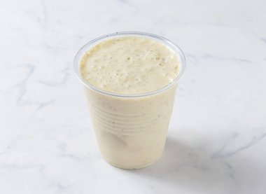 Mermer bir yüzey üzerinde berrak plastik bardakta Satsuma Milkshake kremalı smoothie, kafe veya restoran menüleri için mükemmel, canlandırıcı ve sağlıklı bir içecek seçeneği sunuyor.