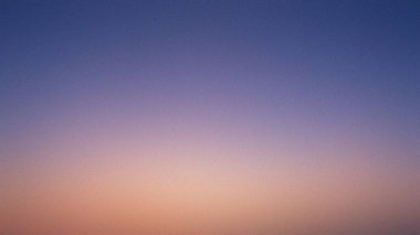 Ufukta şeftaliye dönüşen mavi rengin ince bir gradyanı, yumuşak bir gökyüzü arkaplanı oluşturur..