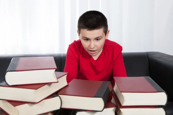 Шокований хлопчик дивиться на багато книг — стокове фото