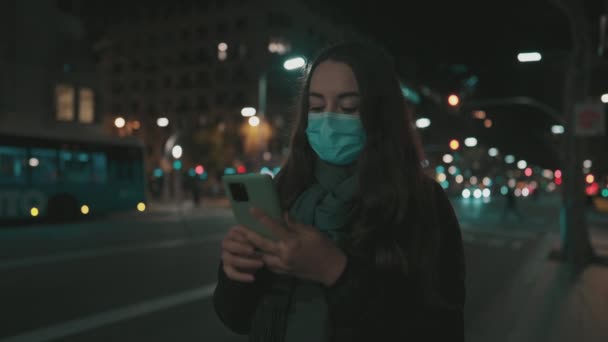 Modello femminile indossando maschera contro il virus, camminando da solo nella città di notte. — Video Stock