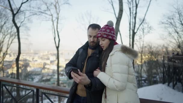 Heureux couple romantique marchant à la journée ensoleillée d'hiver et regardant sur smartphone. — Video