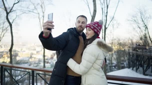 Feliz casal romântico alegre no dia ensolarado de inverno. Eles fazem uma selfie em um smartphone — Vídeo de Stock