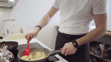 Genç adam mutfakta soğan pişiriyor.