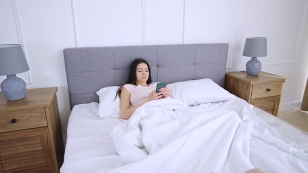 Kvinna som ligger i sängen med mobiltelefon — Stockvideo