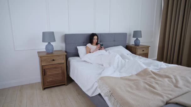 Jong meisje ligt in bed met smartphone — Stockvideo