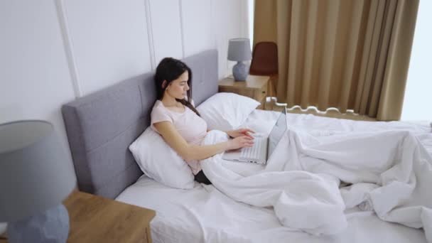 Jong meisje ligt in bed met laptop — Stockvideo